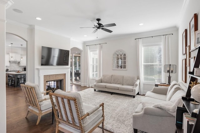 living room featuring ornamental molding, recessed lighting, a tile fireplace, wood finished floors, and arched walkways