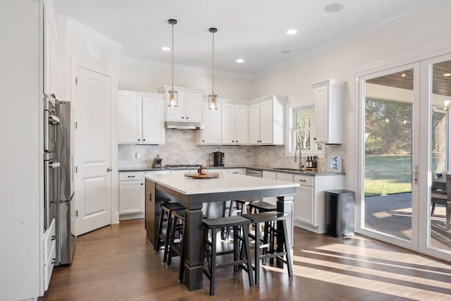 kitchen with under cabinet range hood, tasteful backsplash, dark wood-style floors, and ornamental molding