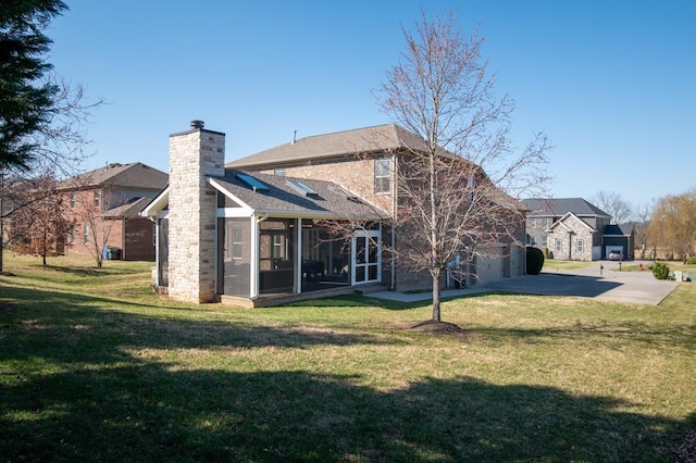 rear view of house with a yard, a garage, a sunroom, and a chimney