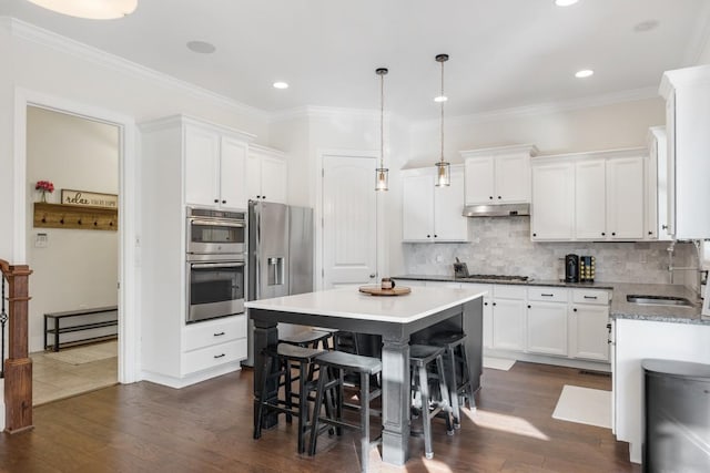 kitchen featuring a kitchen island, under cabinet range hood, white cabinets, stainless steel appliances, and a sink