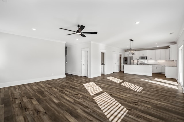 unfurnished living room featuring crown molding, baseboards, dark wood-type flooring, recessed lighting, and a sink