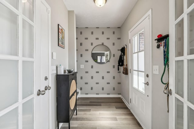 foyer with light wood finished floors, a healthy amount of sunlight, wallpapered walls, and baseboards