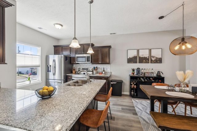 kitchen featuring a breakfast bar area, a sink, stainless steel appliances, dark brown cabinetry, and tasteful backsplash