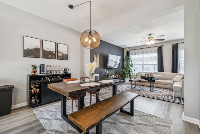 dining room with a ceiling fan, wood finished floors, baseboards, and a textured ceiling