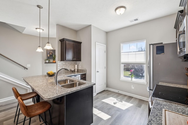 kitchen featuring light wood finished floors, a sink, dark brown cabinets, a kitchen breakfast bar, and tasteful backsplash