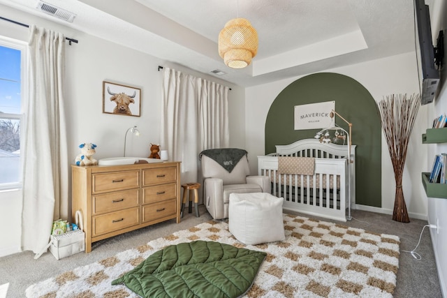 bedroom featuring visible vents, a raised ceiling, carpet, and a crib