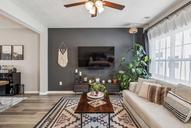 living area featuring visible vents, ceiling fan, baseboards, wood finished floors, and a textured ceiling