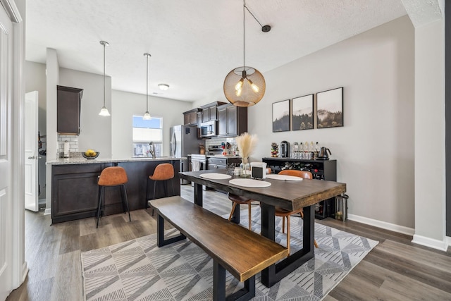 dining area featuring baseboards, light wood finished floors, and a textured ceiling