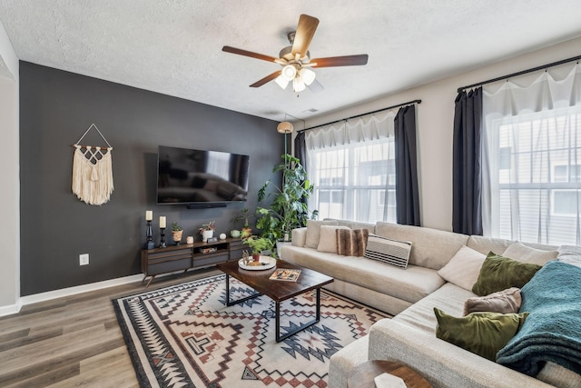 living room with baseboards, a textured ceiling, wood finished floors, and a ceiling fan