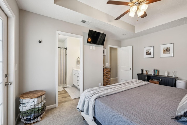 bedroom with visible vents, ensuite bathroom, a tray ceiling, baseboards, and light colored carpet