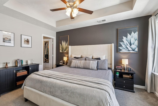 bedroom with visible vents, baseboards, ceiling fan, a raised ceiling, and light colored carpet