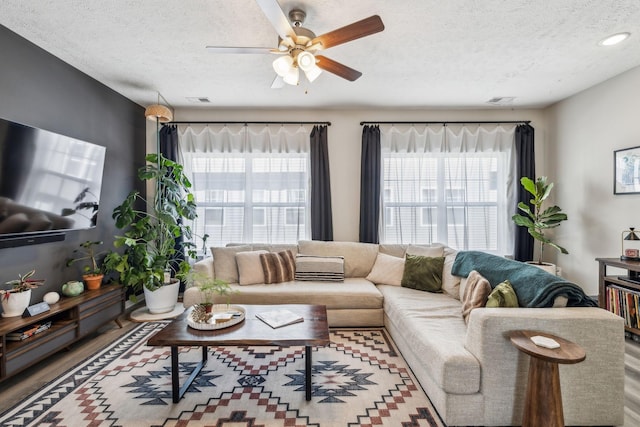 living area featuring visible vents, a textured ceiling, a ceiling fan, and wood finished floors