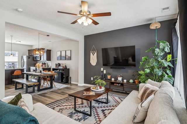 living room featuring visible vents, a textured ceiling, wood finished floors, baseboards, and ceiling fan