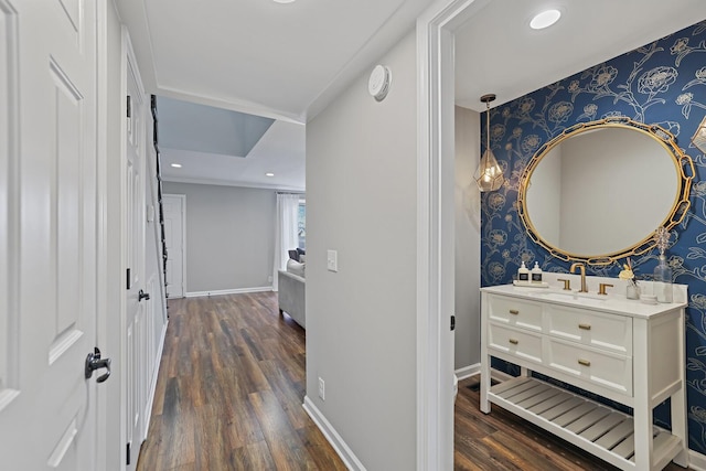 hall featuring dark wood-style flooring, wallpapered walls, baseboards, and a sink