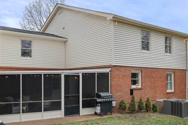 rear view of property with central air condition unit, brick siding, and a sunroom