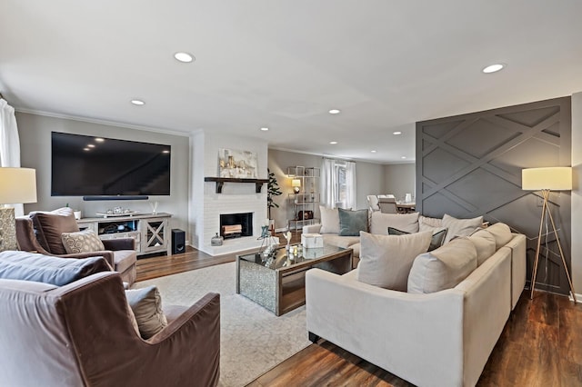 living room featuring ornamental molding, recessed lighting, dark wood-style flooring, and a large fireplace