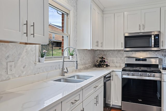 kitchen with light stone counters, white cabinetry, stainless steel appliances, and a sink