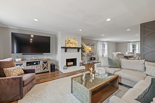 living room with a brick fireplace, recessed lighting, wood finished floors, and ornamental molding