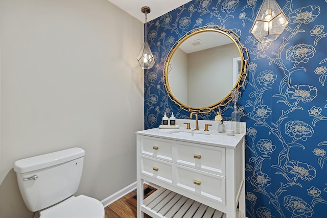 bathroom featuring vanity, wood finished floors, baseboards, wallpapered walls, and toilet