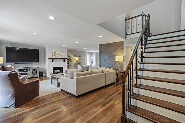 living area with a brick fireplace, crown molding, stairway, recessed lighting, and dark wood-style flooring