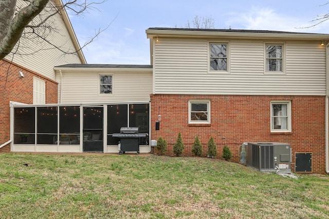 rear view of house with central air condition unit, a lawn, brick siding, and a sunroom