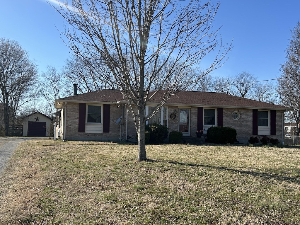 single story home featuring aphalt driveway, a front yard, an outbuilding, and brick siding