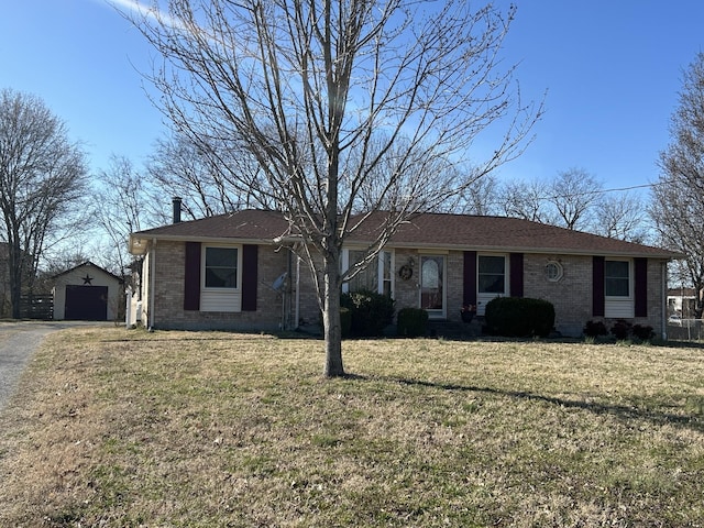 single story home featuring aphalt driveway, a front yard, an outbuilding, and brick siding