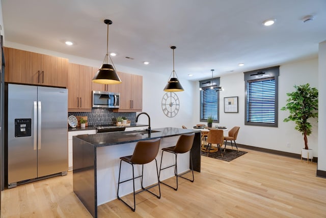 kitchen with a breakfast bar, an island with sink, a sink, appliances with stainless steel finishes, and tasteful backsplash