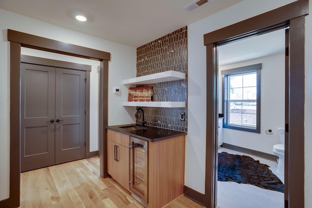 kitchen with tasteful backsplash, visible vents, beverage cooler, light wood-type flooring, and a sink