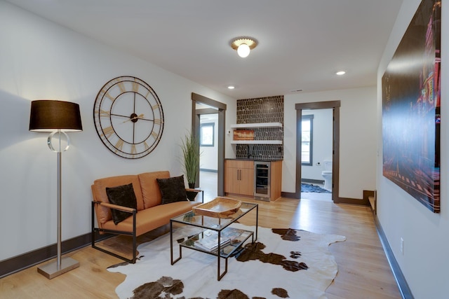 living room featuring baseboards, wine cooler, indoor bar, and light wood-style flooring