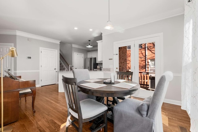 dining room featuring light wood-type flooring, visible vents, ornamental molding, and stairs