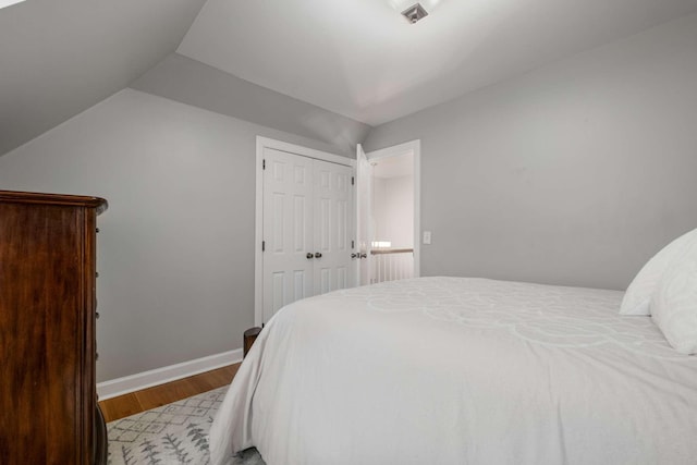 bedroom with a closet, baseboards, lofted ceiling, and wood finished floors