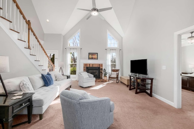 living area with stairway, light carpet, a fireplace, high vaulted ceiling, and a ceiling fan