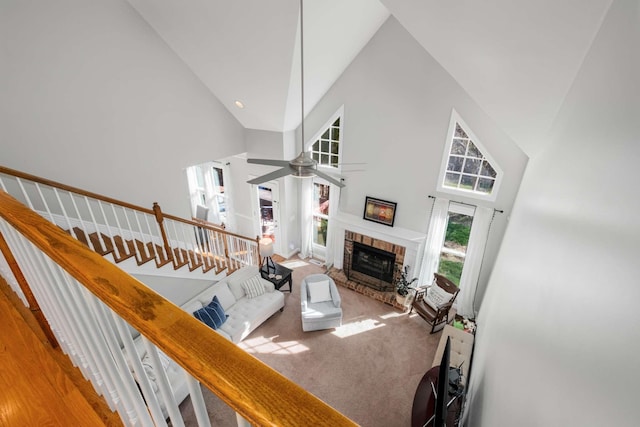 living area featuring high vaulted ceiling, a fireplace, ceiling fan, stairs, and carpet flooring