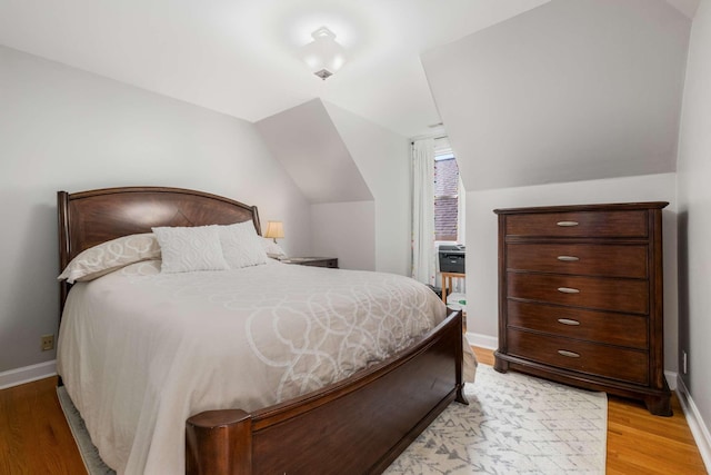 bedroom with light wood finished floors, baseboards, and vaulted ceiling