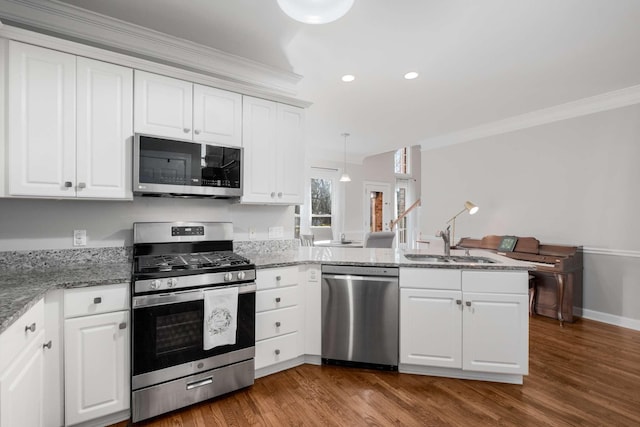 kitchen with a sink, appliances with stainless steel finishes, a peninsula, white cabinets, and dark wood-style flooring