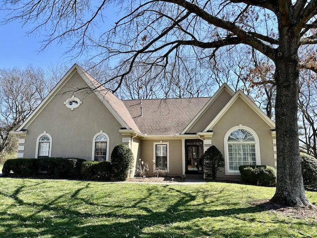 view of front facade with stucco siding, a front lawn, and roof with shingles