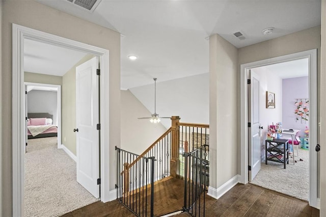 hallway with visible vents, an upstairs landing, baseboards, and dark wood finished floors