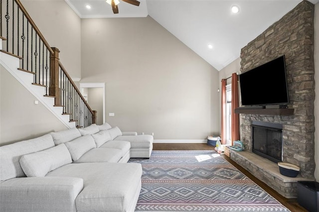 living area with ceiling fan, baseboards, stairway, a stone fireplace, and dark wood-style flooring