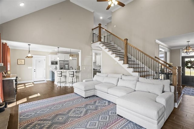 living area featuring dark wood-type flooring, ornamental molding, ceiling fan with notable chandelier, stairway, and baseboards