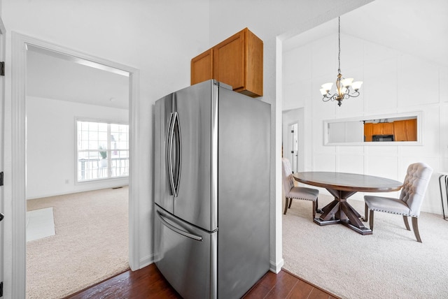 kitchen with brown cabinets, freestanding refrigerator, a notable chandelier, dark colored carpet, and dark wood-style flooring