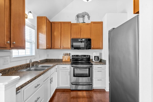 kitchen with dark countertops, vaulted ceiling, dark wood-style floors, stainless steel appliances, and a sink