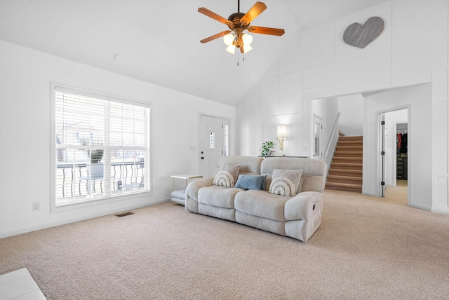 living area with visible vents, light carpet, high vaulted ceiling, ceiling fan, and stairs