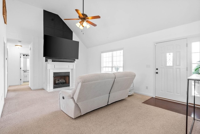 living area featuring baseboards, high vaulted ceiling, a fireplace with flush hearth, ceiling fan, and light carpet