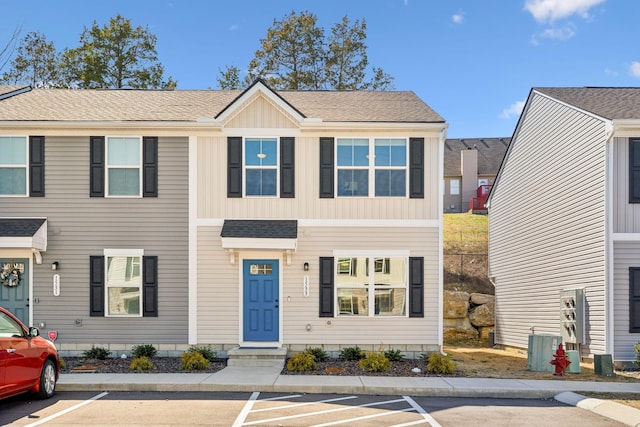 townhome / multi-family property featuring board and batten siding, central AC unit, uncovered parking, and roof with shingles