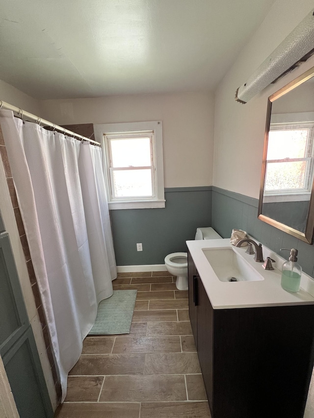 full bath featuring wood finish floors, a wainscoted wall, toilet, a shower with shower curtain, and vanity