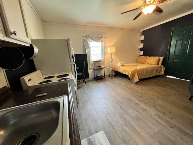 bedroom featuring a ceiling fan, wood finished floors, freestanding refrigerator, a sink, and ornamental molding