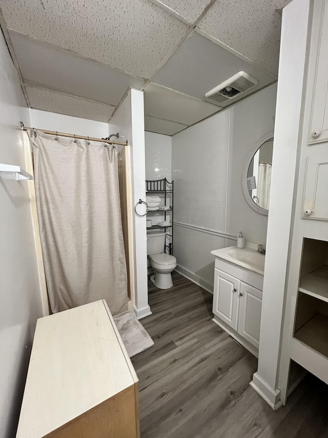 full bath with vanity, wood finished floors, visible vents, a paneled ceiling, and toilet