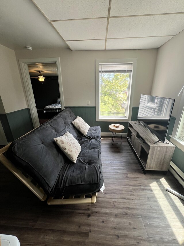 living area with a drop ceiling, wainscoting, and wood finished floors