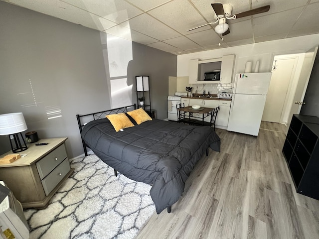 bedroom with light wood finished floors, a drop ceiling, and freestanding refrigerator